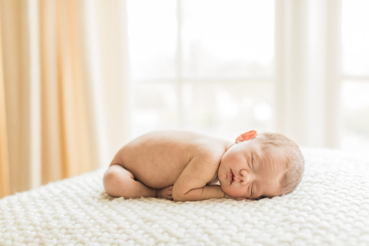 newborn baby is curled up with her bottom sticking in the air and her head resting on her hands