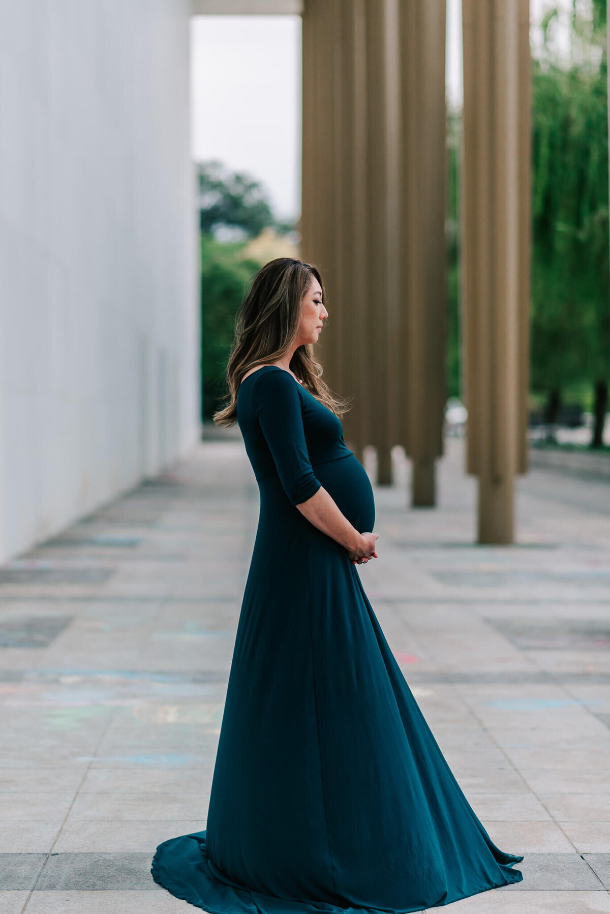 An expecting asian woman wearing a blue-green maternity gown against the Kennedy Center backdrop