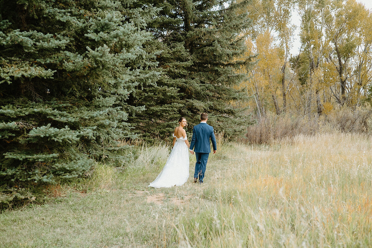 bride and groom walking through the trees on wedding day in Colorado
