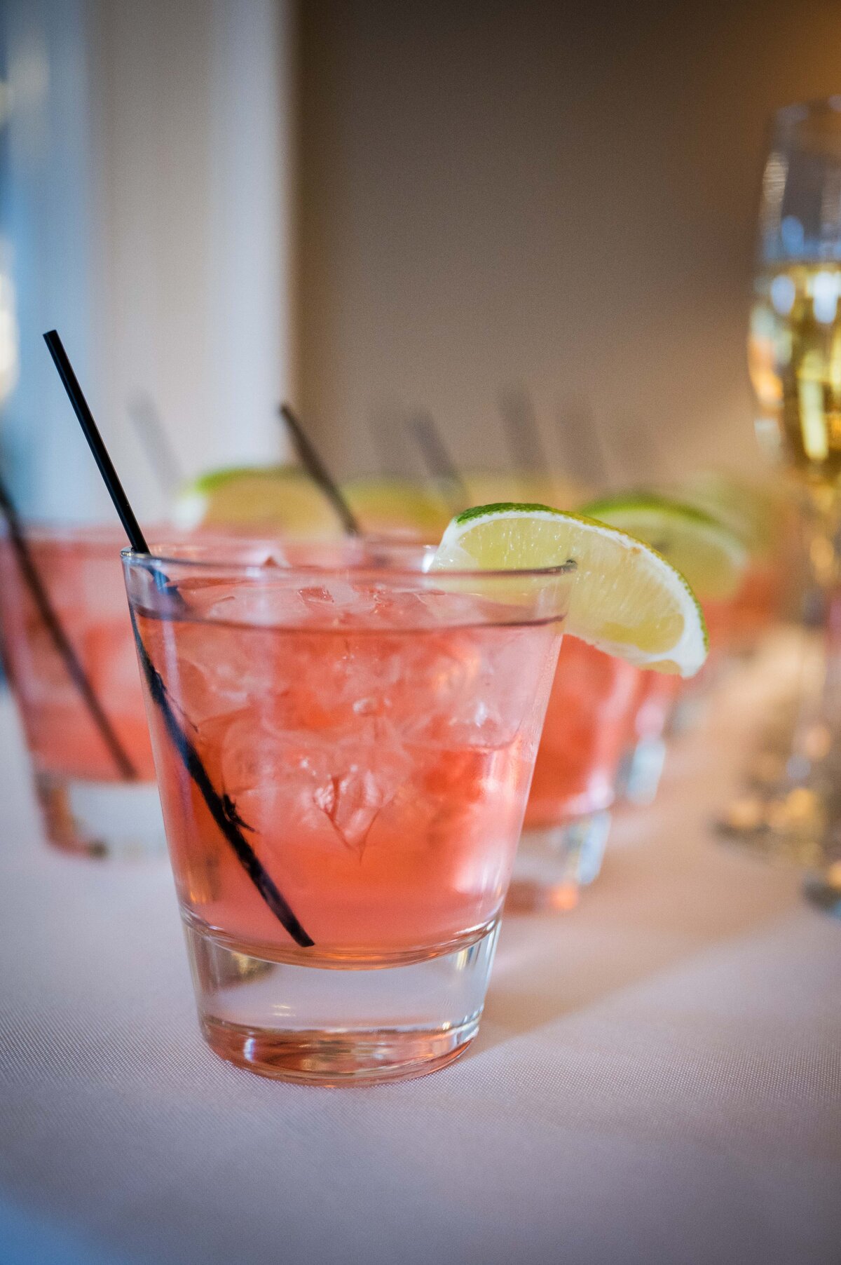 A close up shot of several fruity pink cocktails with lime wedges on the glass rim.