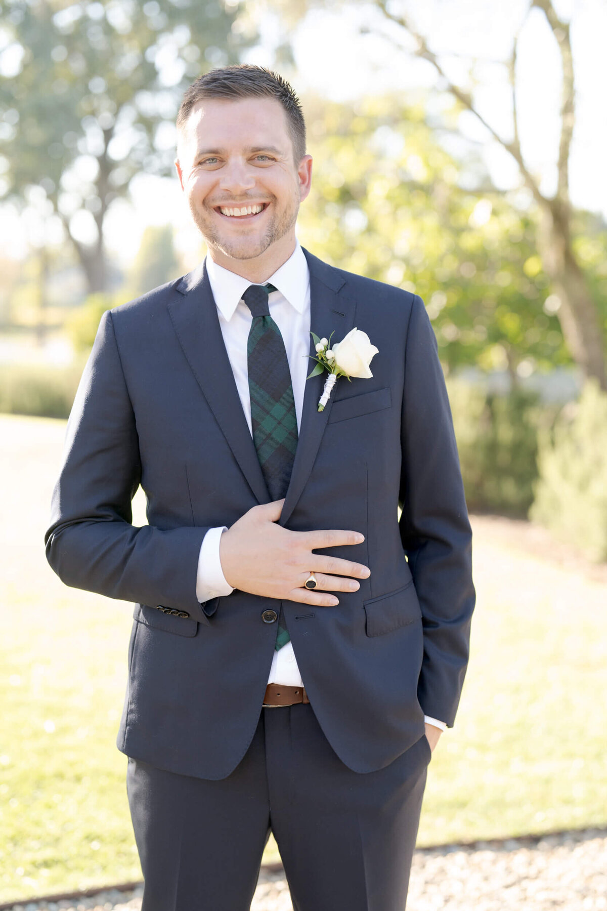 A happy bridegroom flaunts his wedding ring and suit in sunny outdoors.