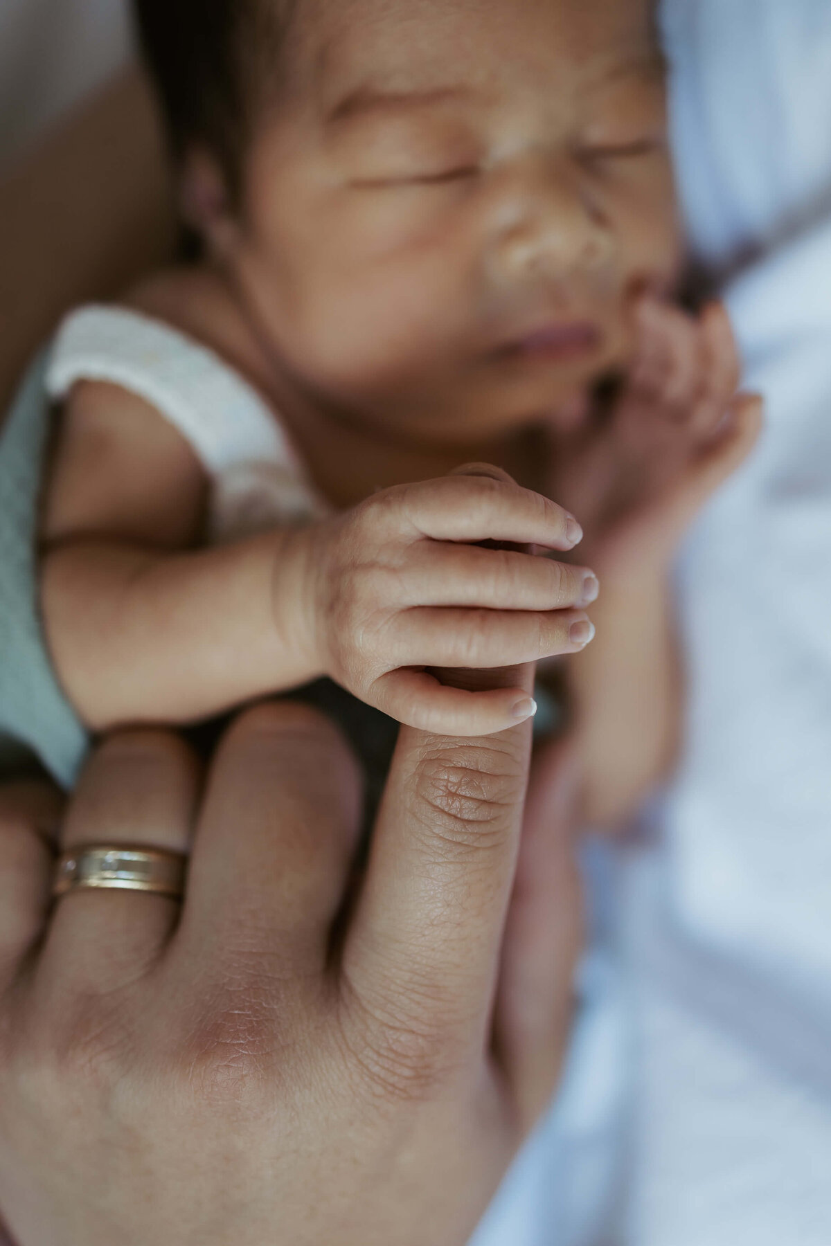 A close up of a newborn baby tightly holding onto her parent's finger as they sleep.