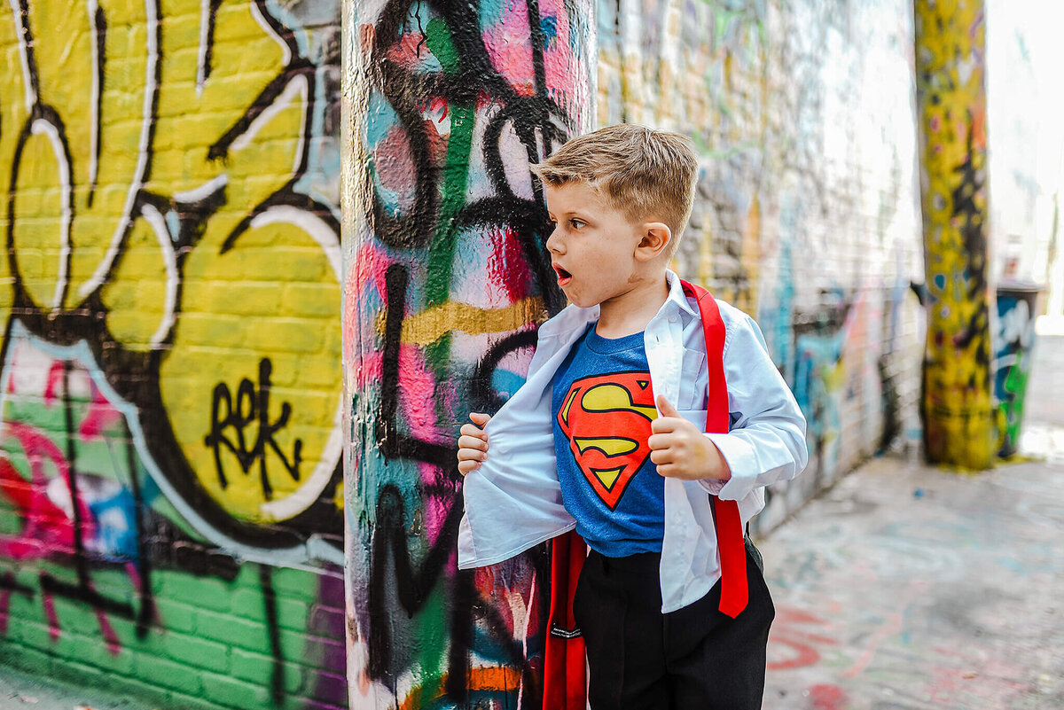 Little boy in a white shirt and black pants wearing a superman shirt in grafiti alley near MICA in Baltimore Maryland