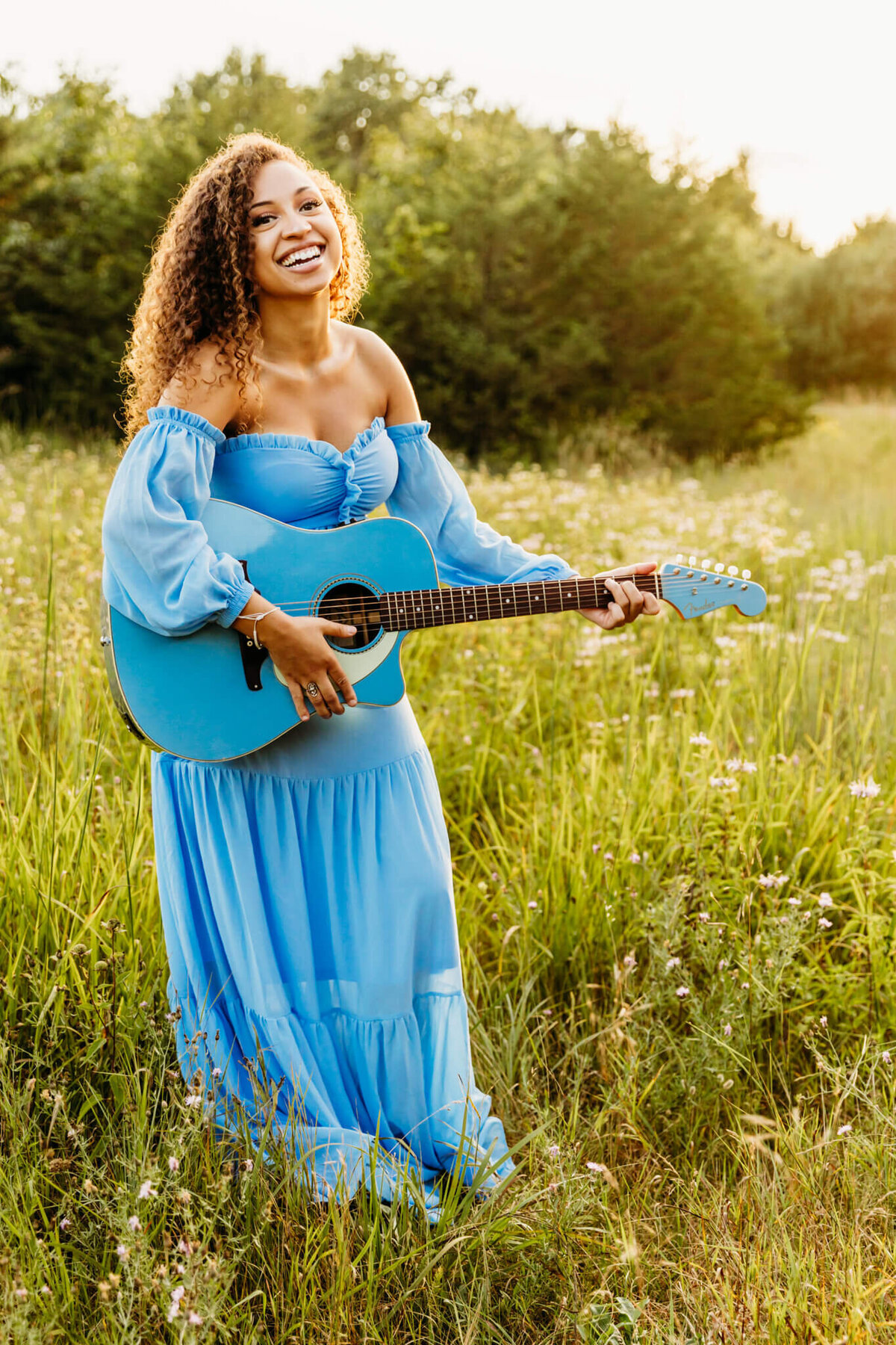 beautiful senior in a blue boho dress laughing while holding blue guitar