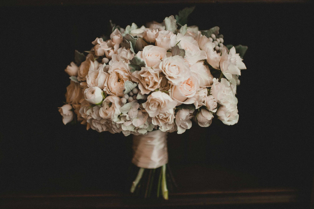Classic round pave bridal bouquet of white roses, ranunculus, silver brunia, and dusty miller.