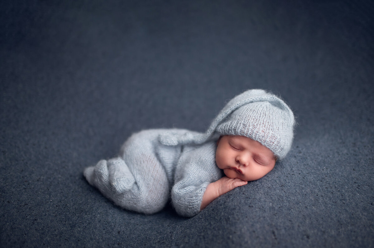 Minimalist portrait of baby boy sleeping in a knit, blue onesie and matching stocking hat in our Waukesha studio.
