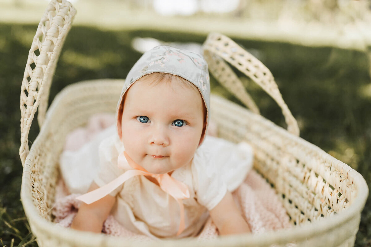 baby charlotte lays on her belly in a moses basket, wearing a bonnet