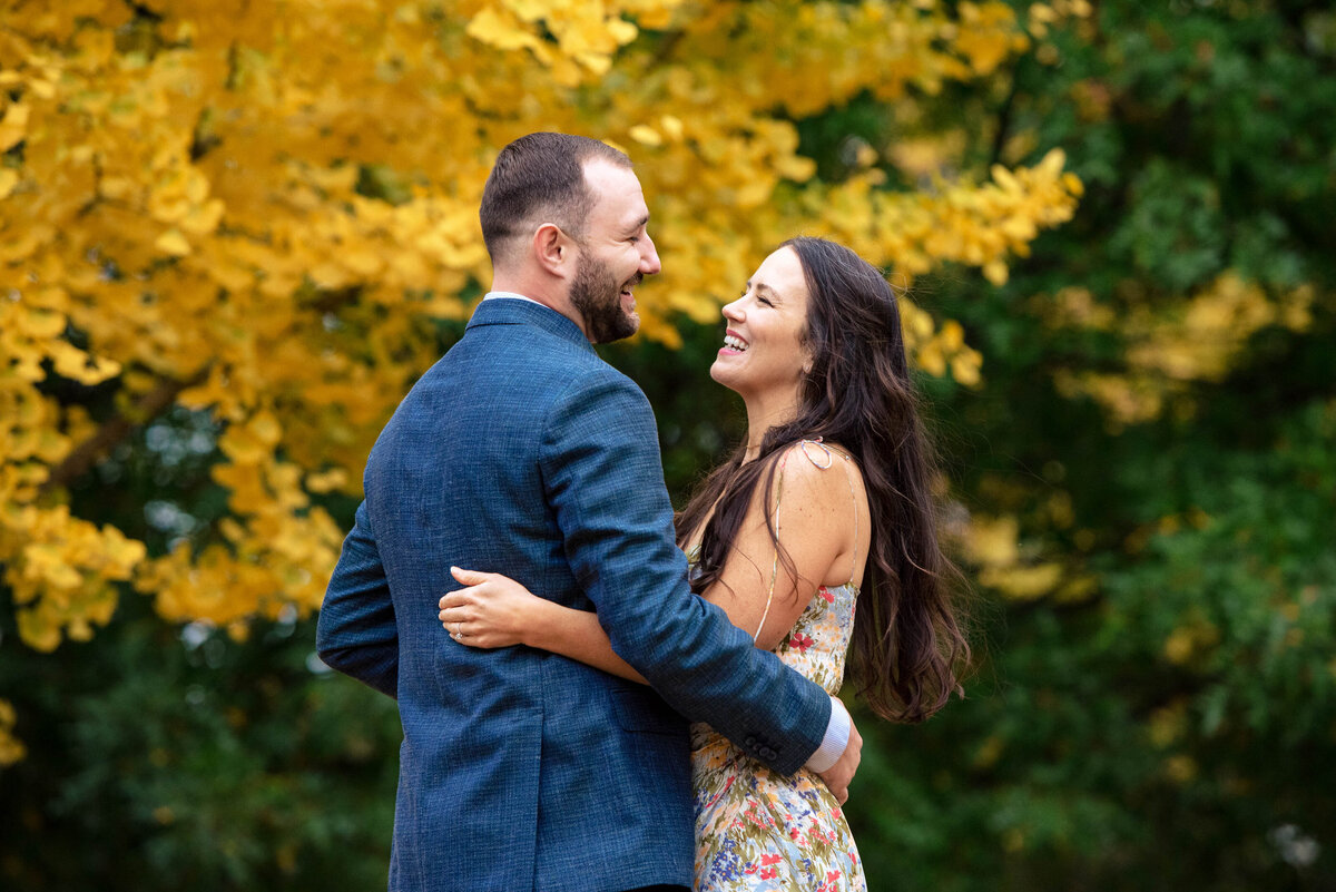 Couple-facing-one-another-laughing-amid-yellow-and-green-fall-leaves-at-Piedmont-Park-in-Atlanta