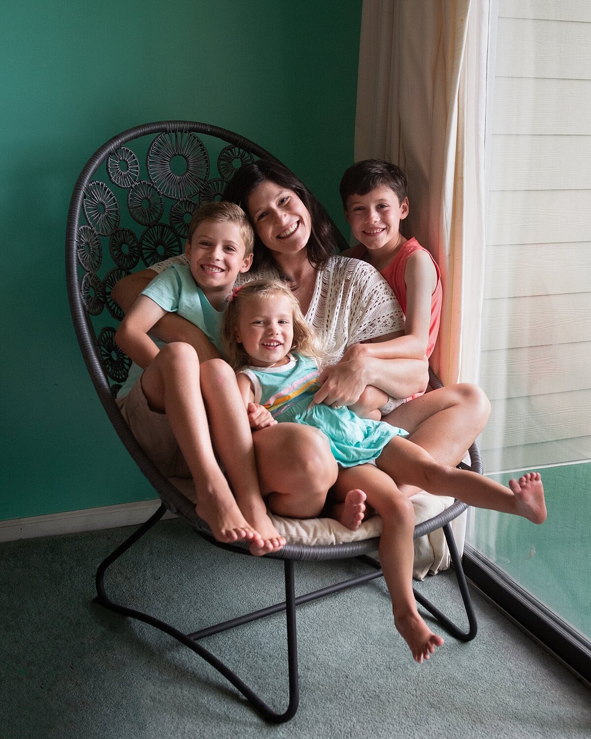 mother in beach chair with three kids on her lap against teal wall