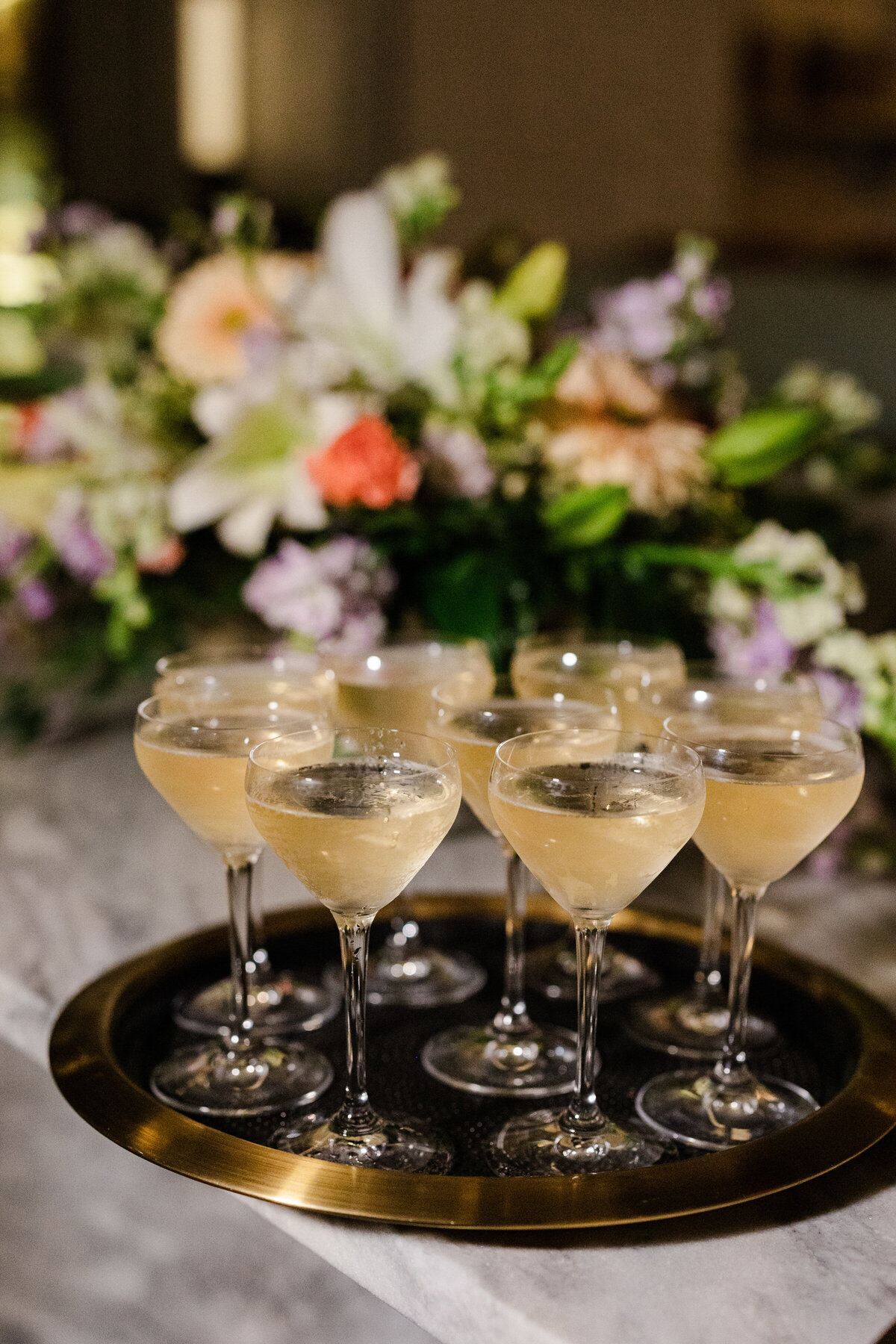 Detail shot of a platter of glasses of champagne at an elopement in Dallas, Texas. The nine glasses all bubble and sit on a golden tray and are backed by a large floral arrangement.