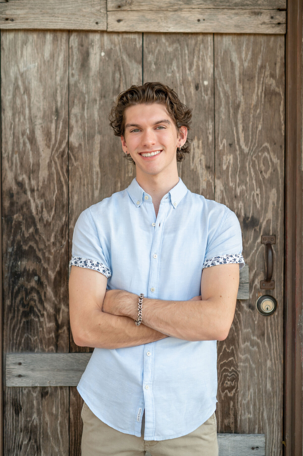High school senior boy in front of wooden door smiles at camera.