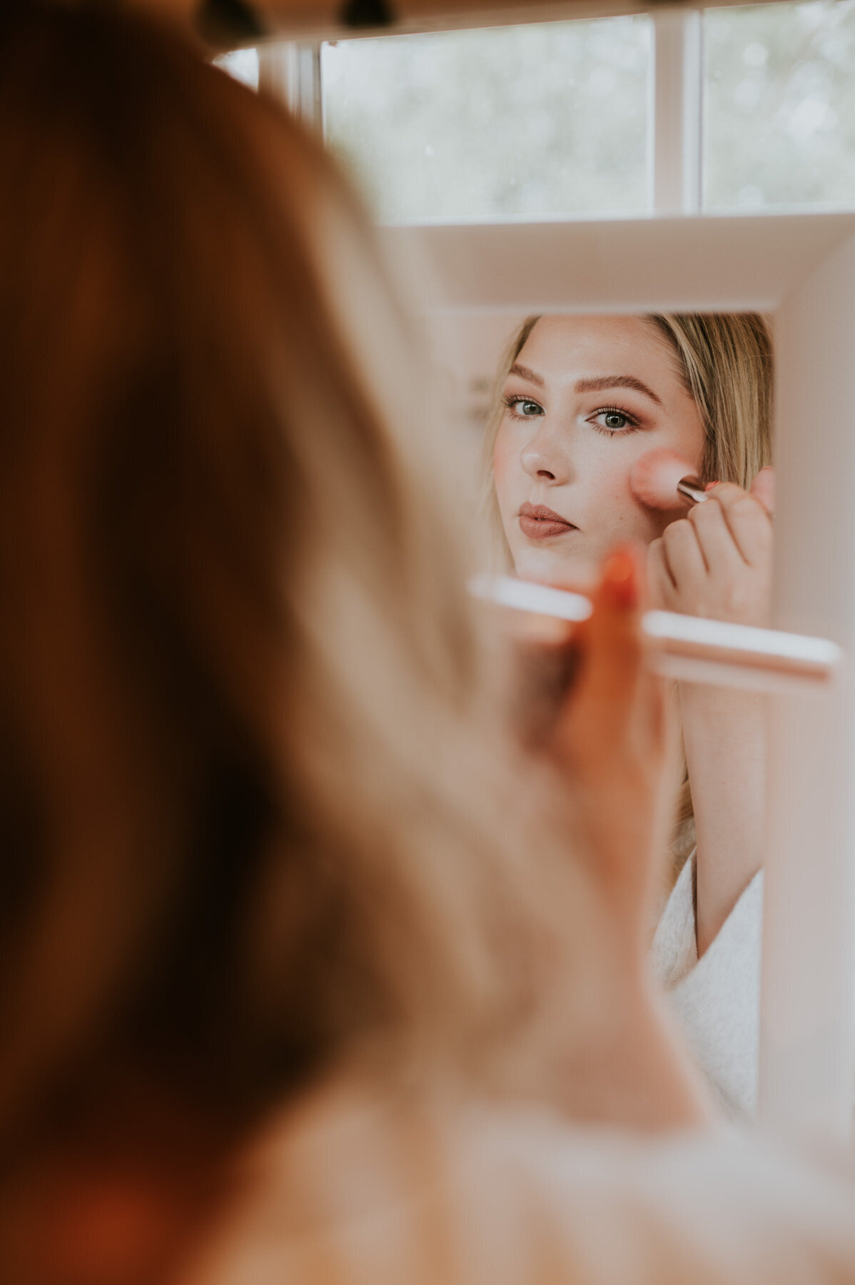 Bride doing her own makeup in front of mirror