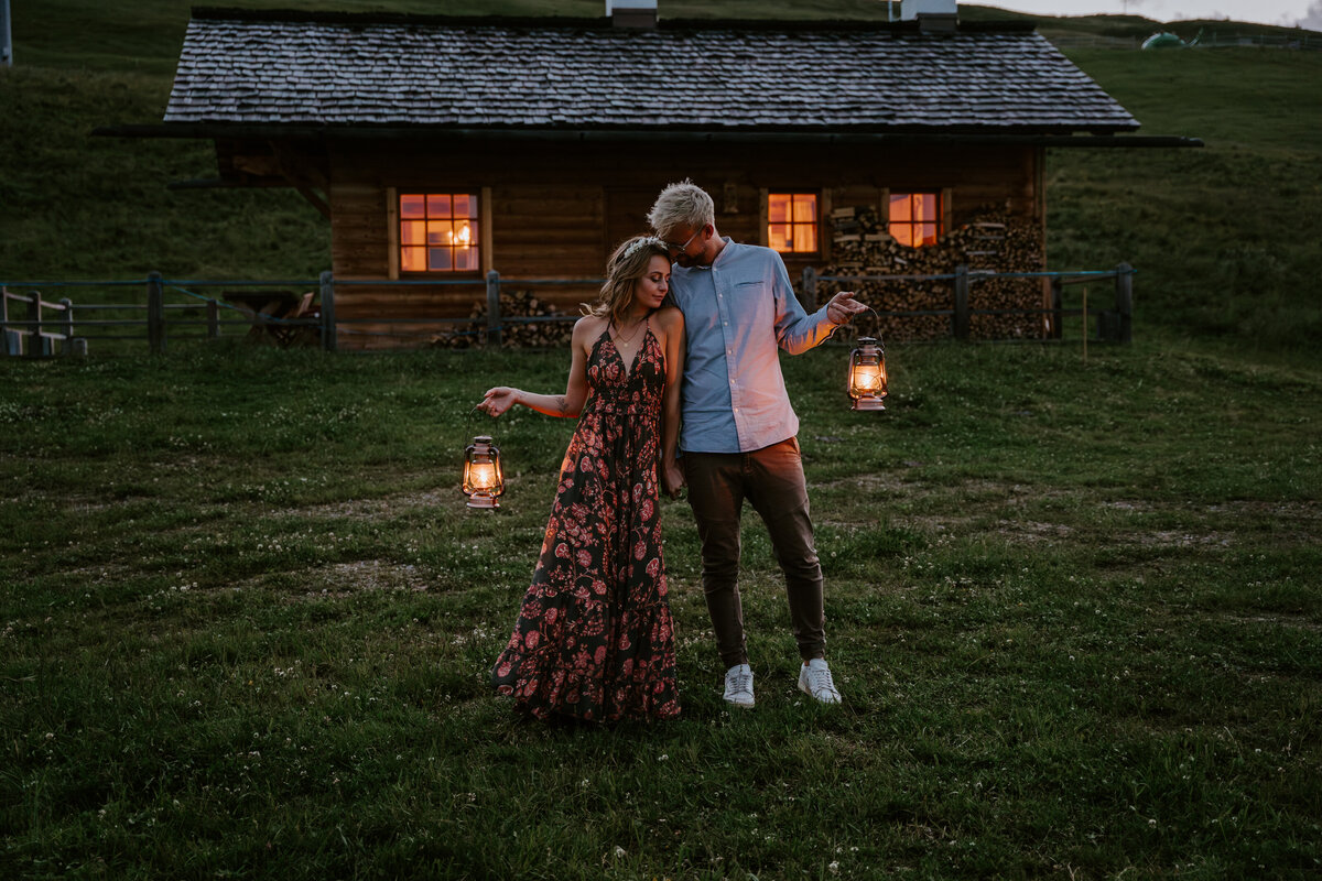 Couple posing with lanterns in front of cozy cabin in Italian Dolomites