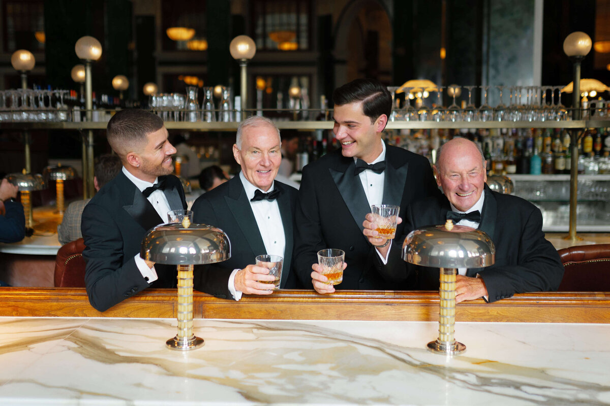 groom with his groomsmen all dressed in black tie enjoying drinks in the bar at the ned hotel London before his chic city wedding