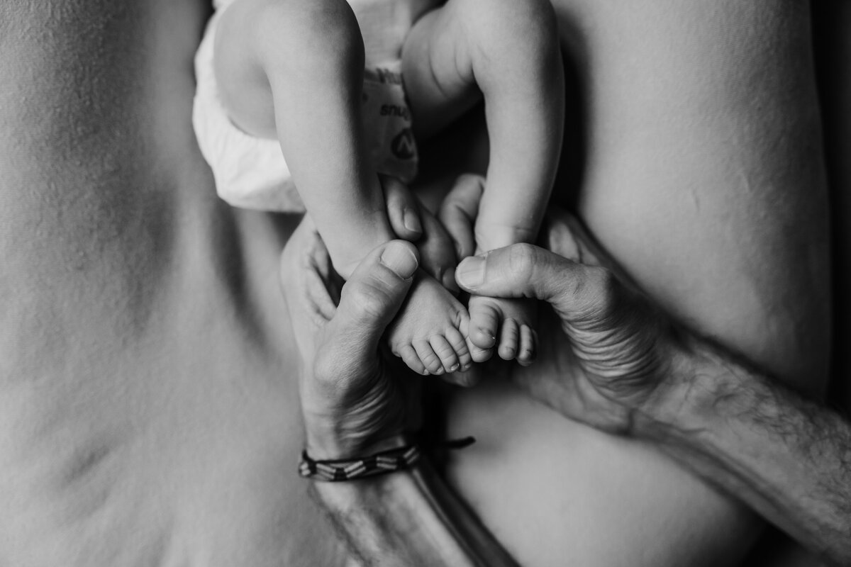 Newborn Photographer, a baby lays on the bed, dad's hand hold his baby toes
