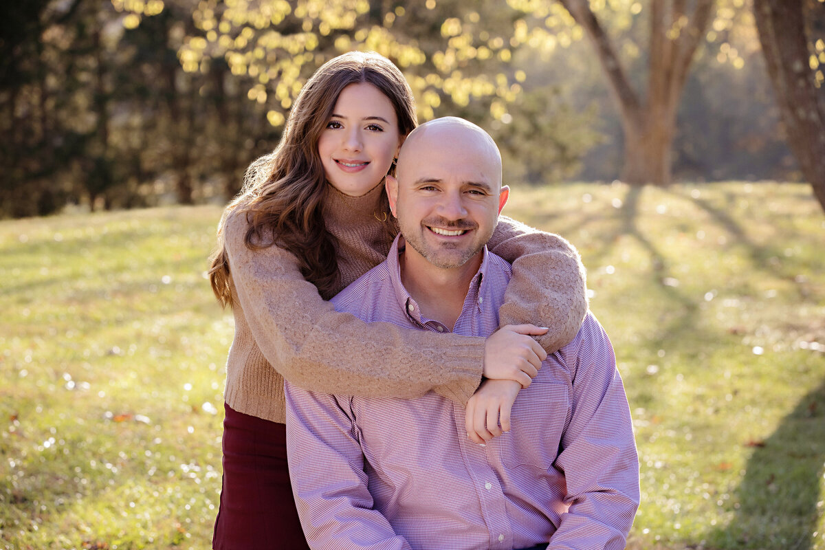 Smiling father and younger daughter embracing in grassy field with hill and tree in autumn at Anne Springs Close Greenway
