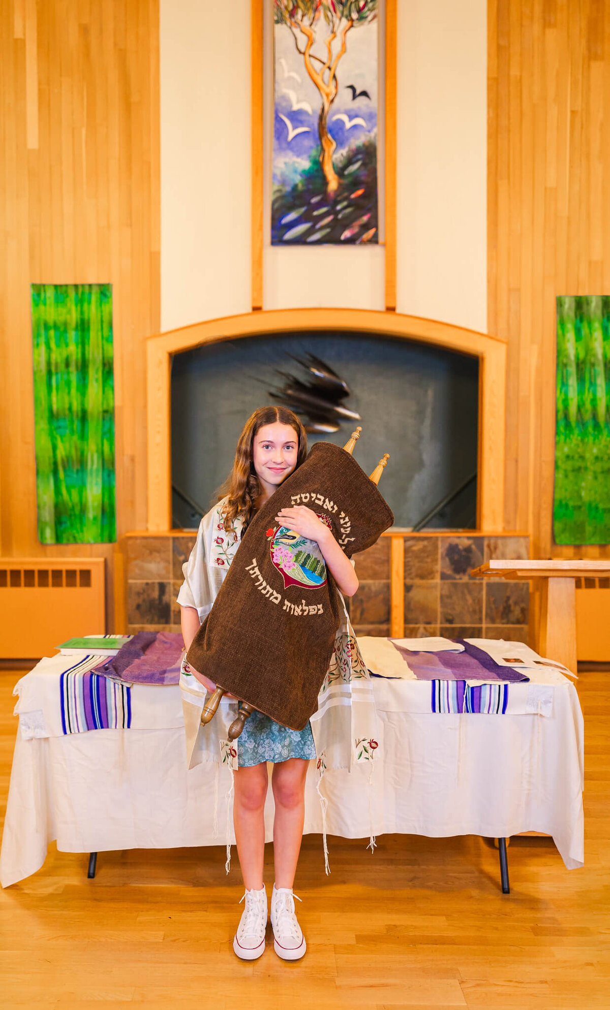 A teen girl stands with the torah in the temple in her tallit and blue floral dress