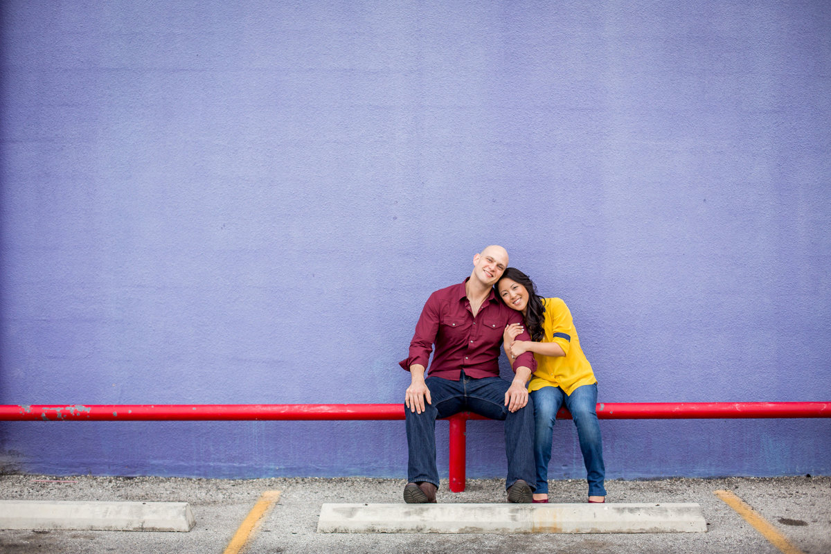 Happily engaged couple sitting on red rail in front of purple wall at Market Square in San Antonio