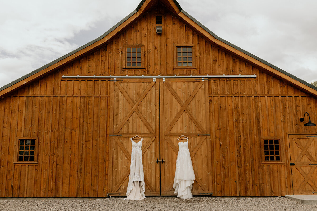 two wedding dresses hanging on a wooden barn