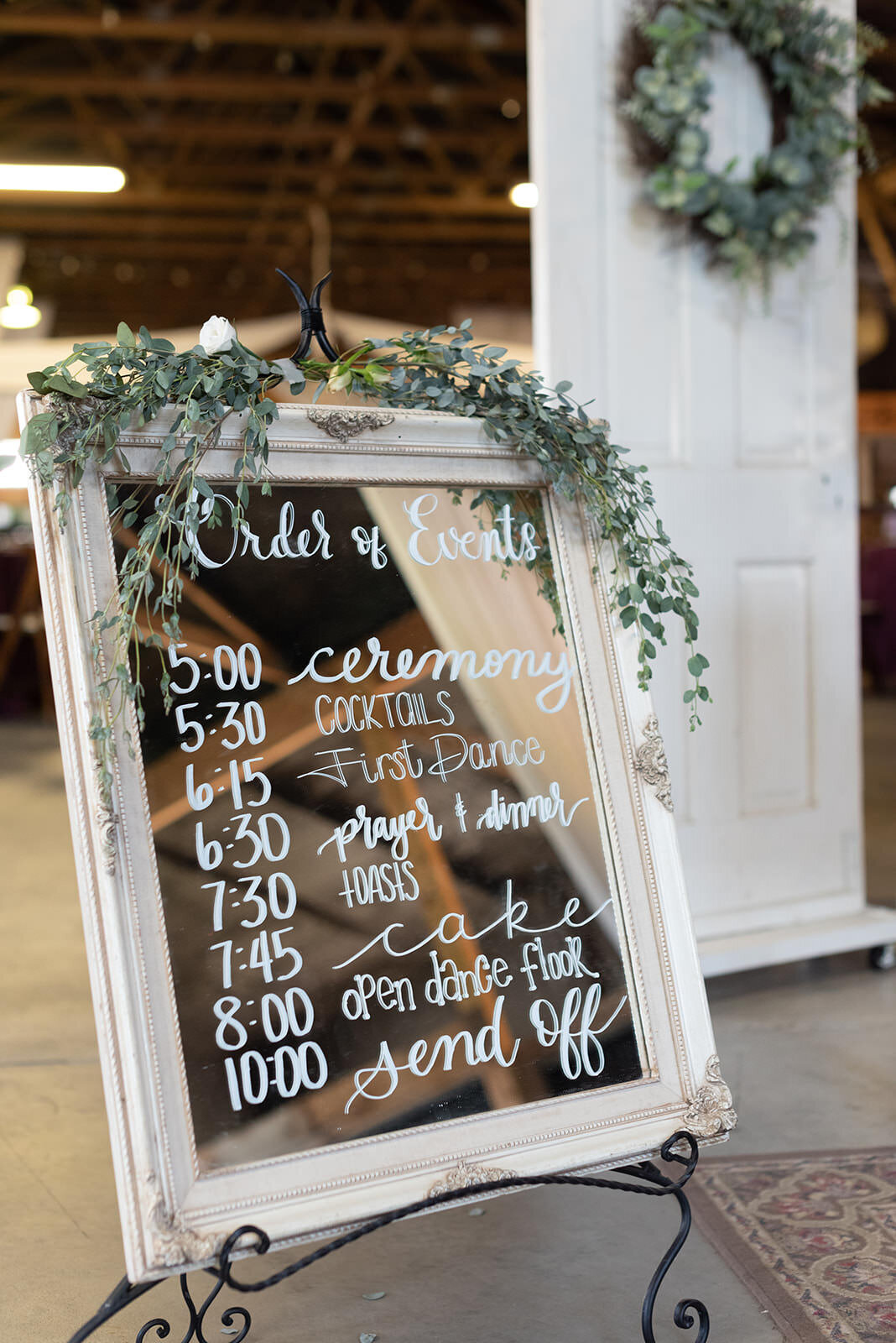 Mirro sign with wedding timeline details accented with greenery ontop