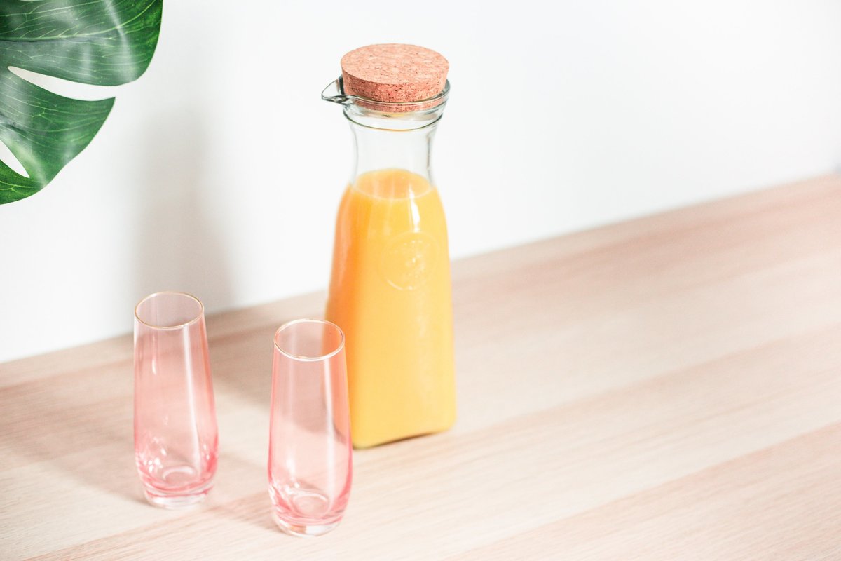 Two pink empty glasses with a pitcher of mimosa sitting on a wooden table