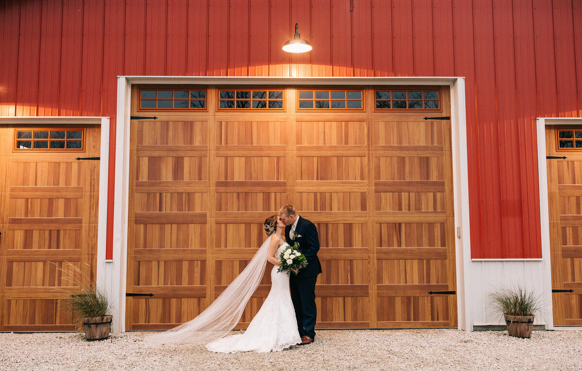 Bride and groom kissing in front of a barn door at their wedding venue