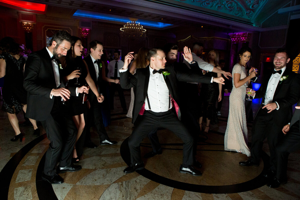 A man in a black suit dances with wedding guests Venetian New Jersey wedding photographer Milestone Images