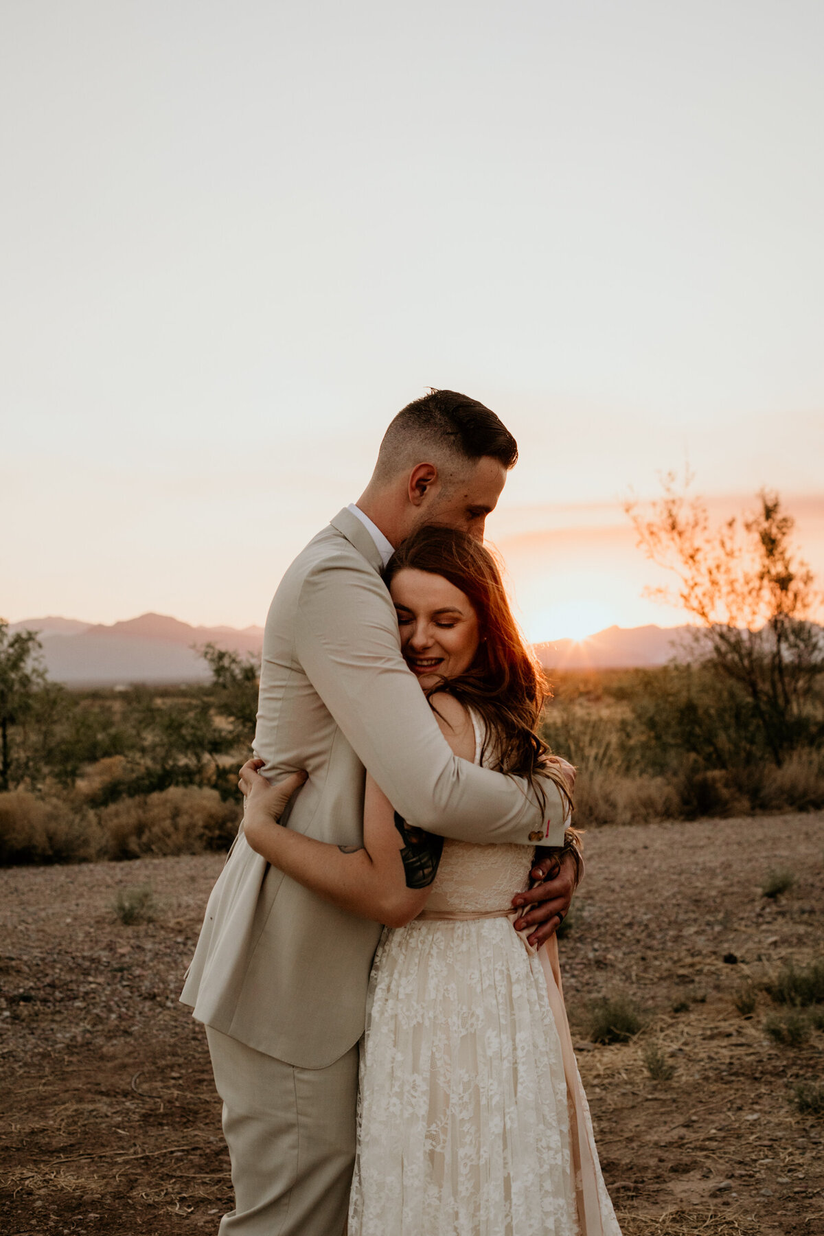 bride and groom hugging each other and laughing at sunset