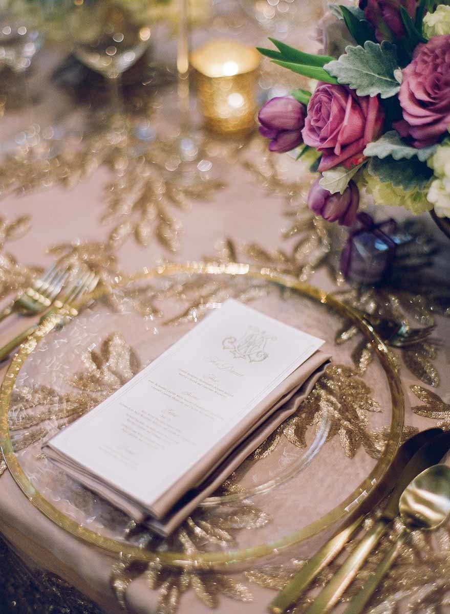Elegant gold place setting paired with purple floral arrangements.