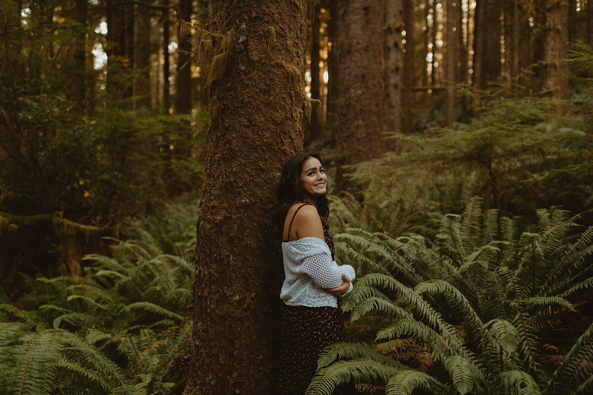 girl leaning against trees in the forest, surrounded by ferns