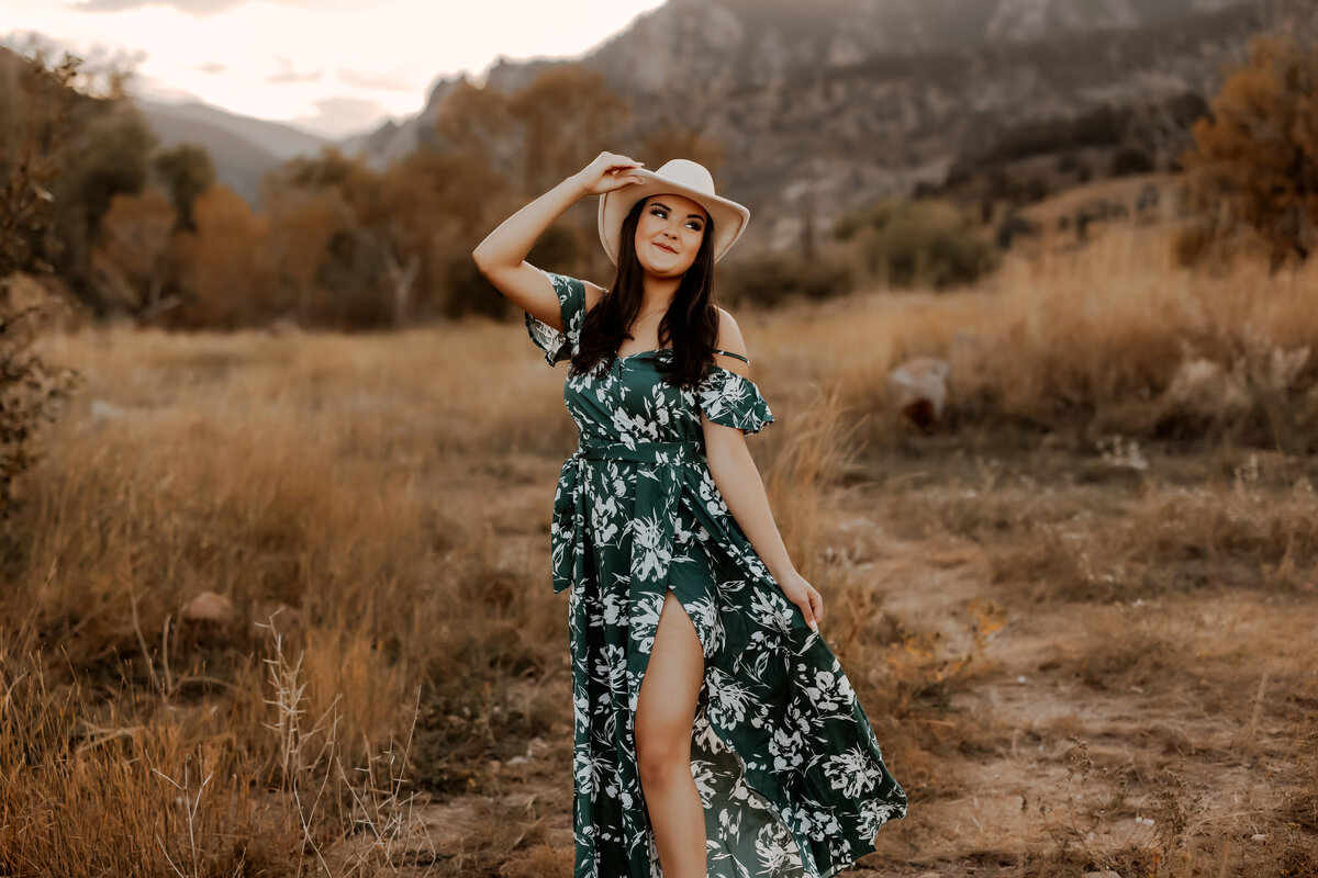 high school girl stands with mountains behind her while wearing a long green dress with a slit in the let