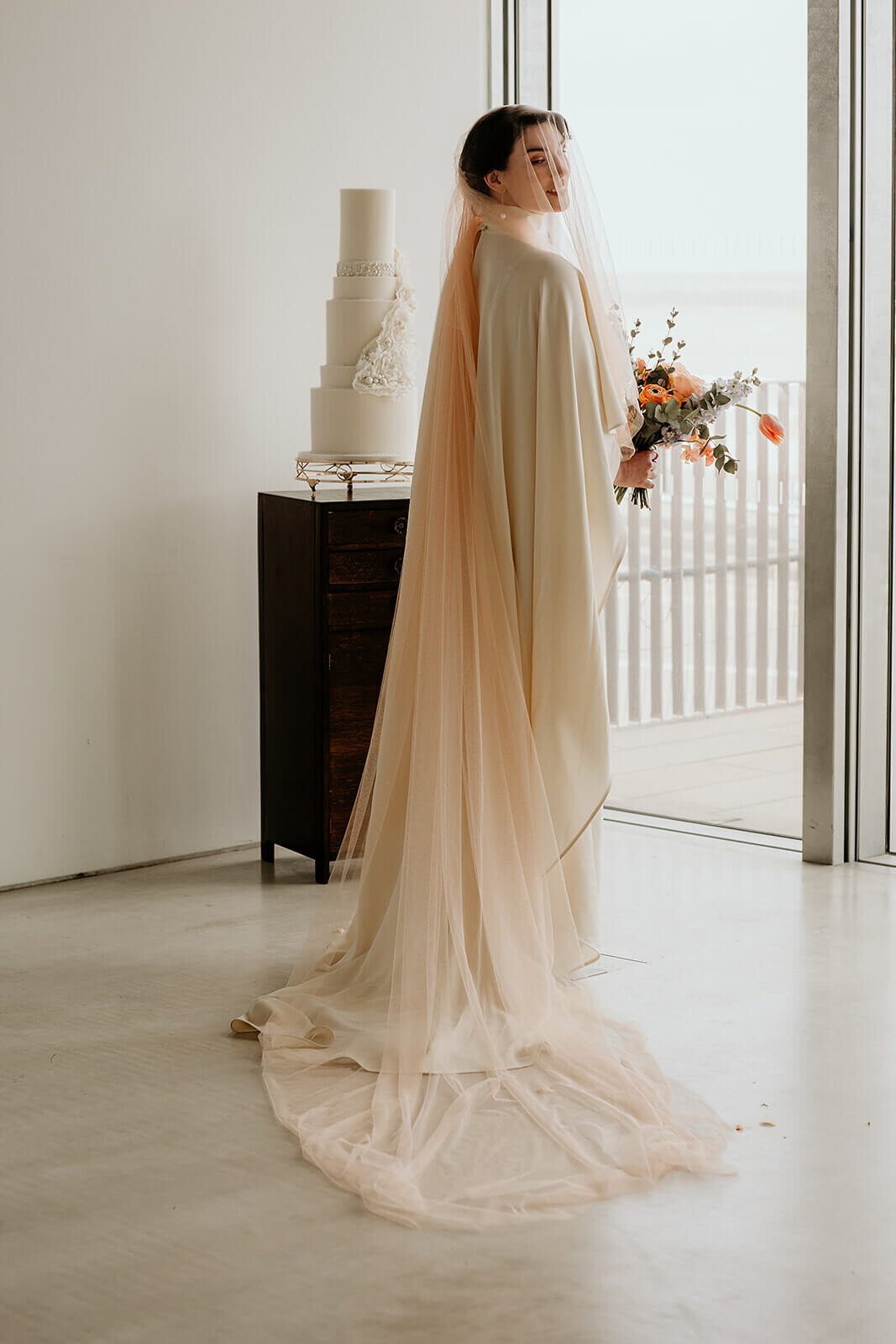 Bride posing in Foyle room.  Floor length peach veil and caped wedding dress