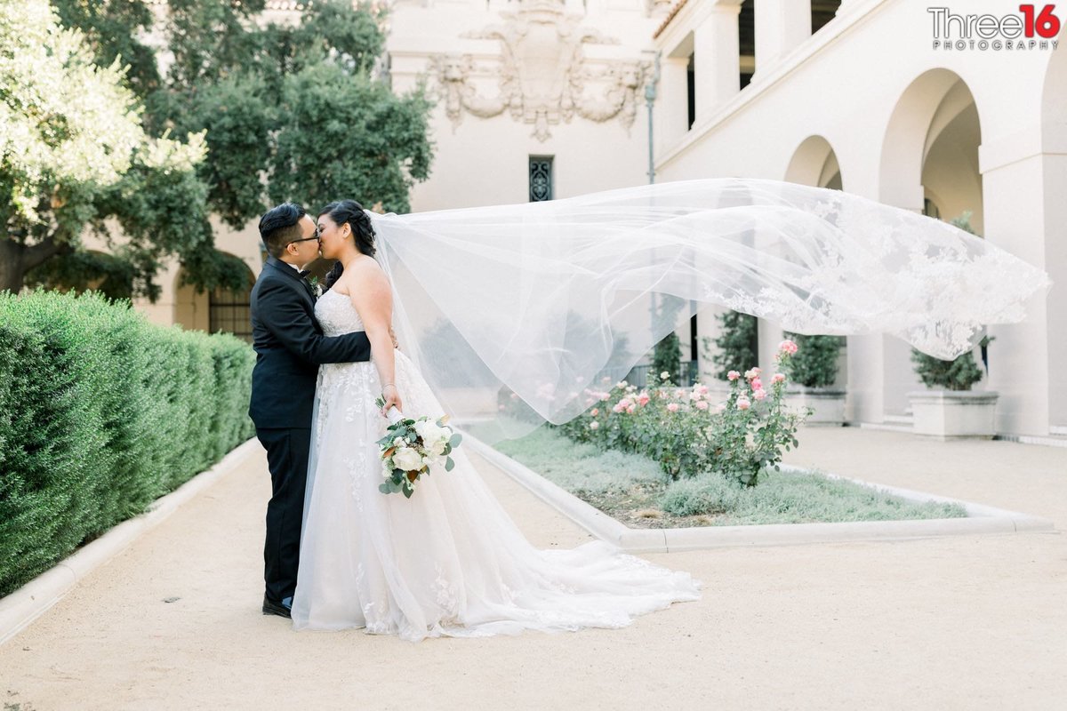 Bride and Groom share a kiss in the courtyard as her veil flies into the wind