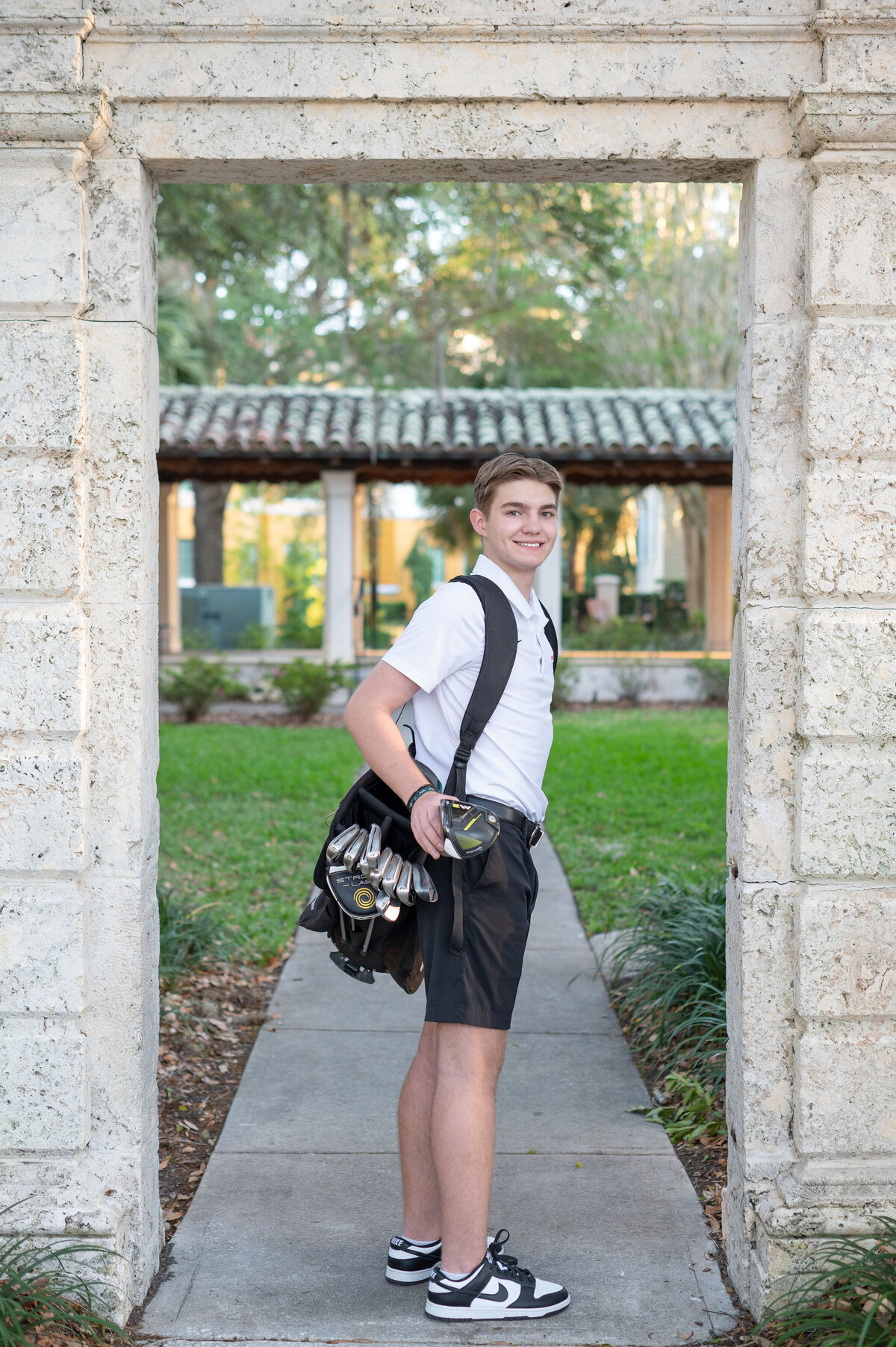 High school senior boy wearing a golf bag looks back to camera smiling.