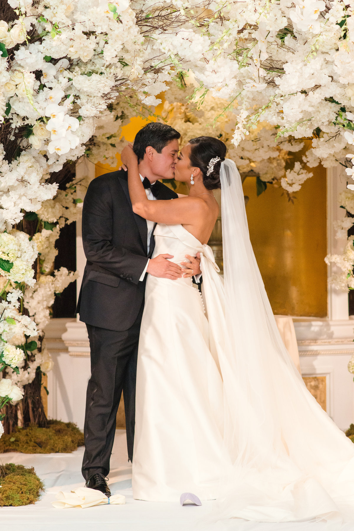 photo of bride and groom kissing under white flowers during wedding at The Garden City Hotel