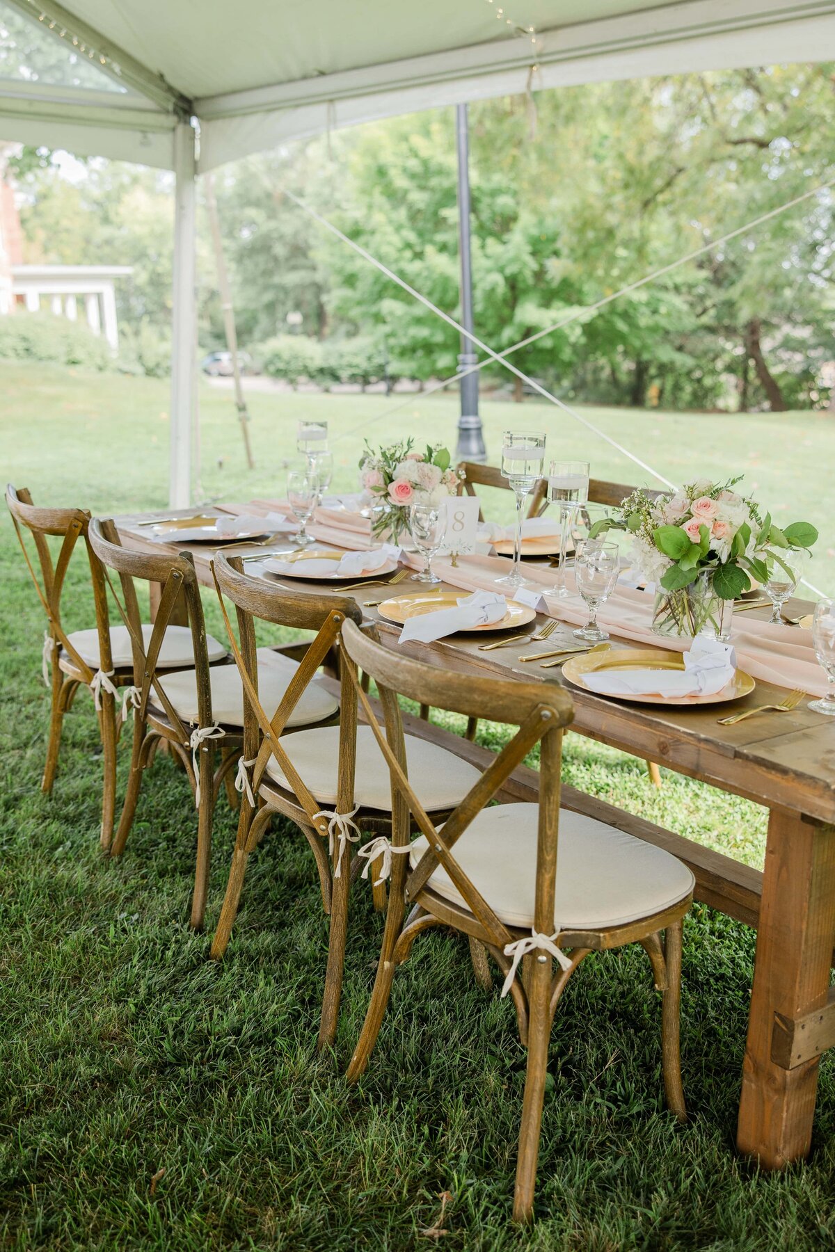 Elegantly set dining table under a tent in the park at Park Farm Winery, complete with wooden chairs, floral centerpieces, and place settings.