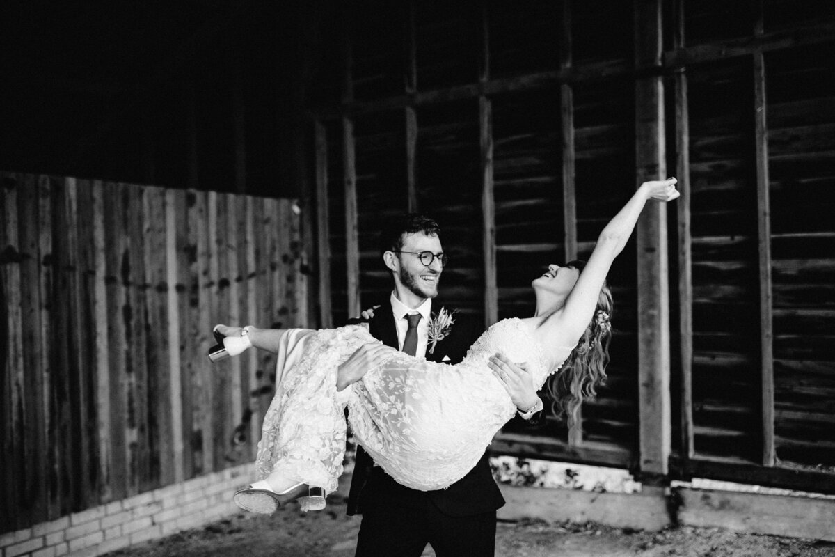 Black and white photo of groom picking up bride in joyful pose