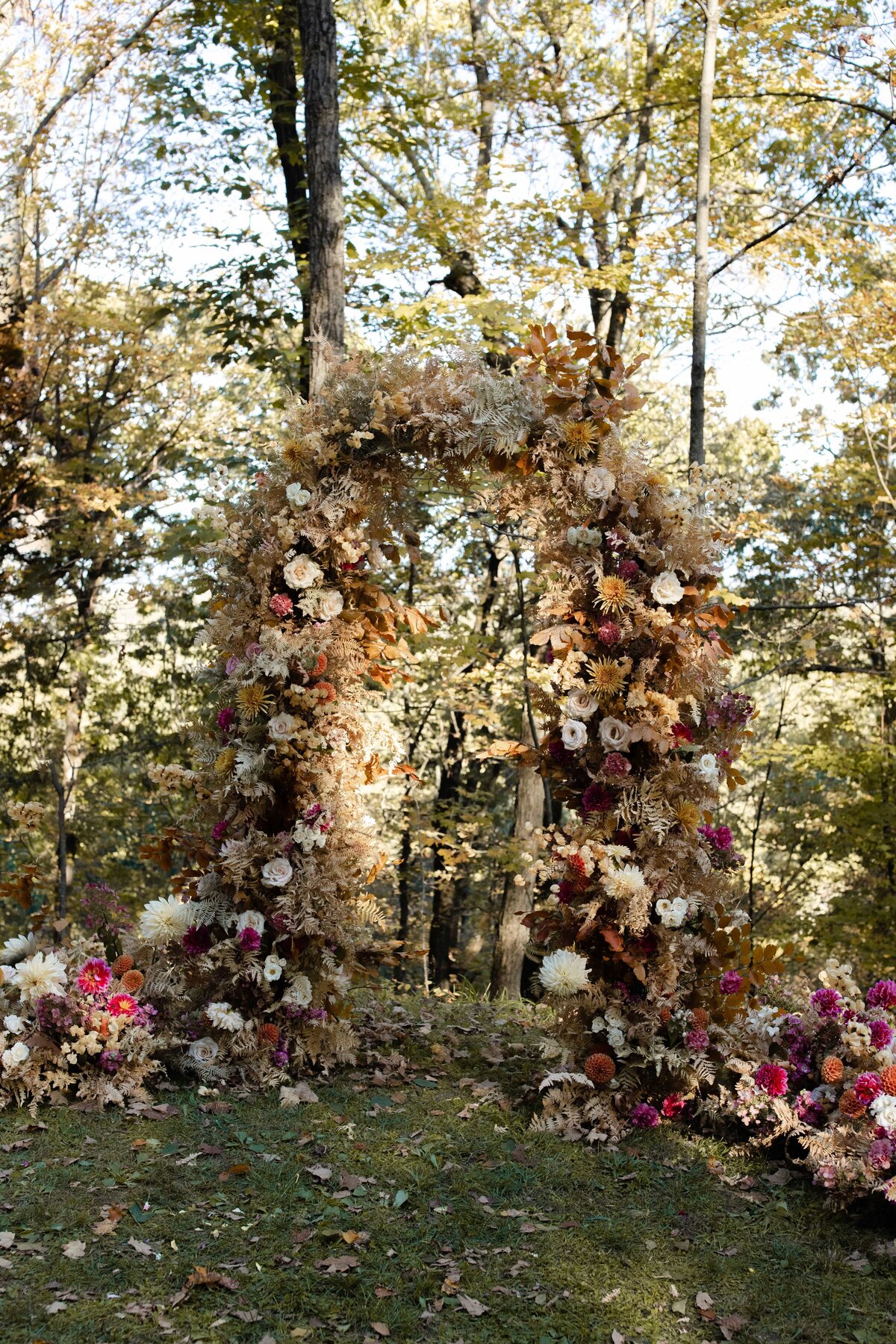 Romantic floral statement design on wedding ceremony arbor outside in wooded area.