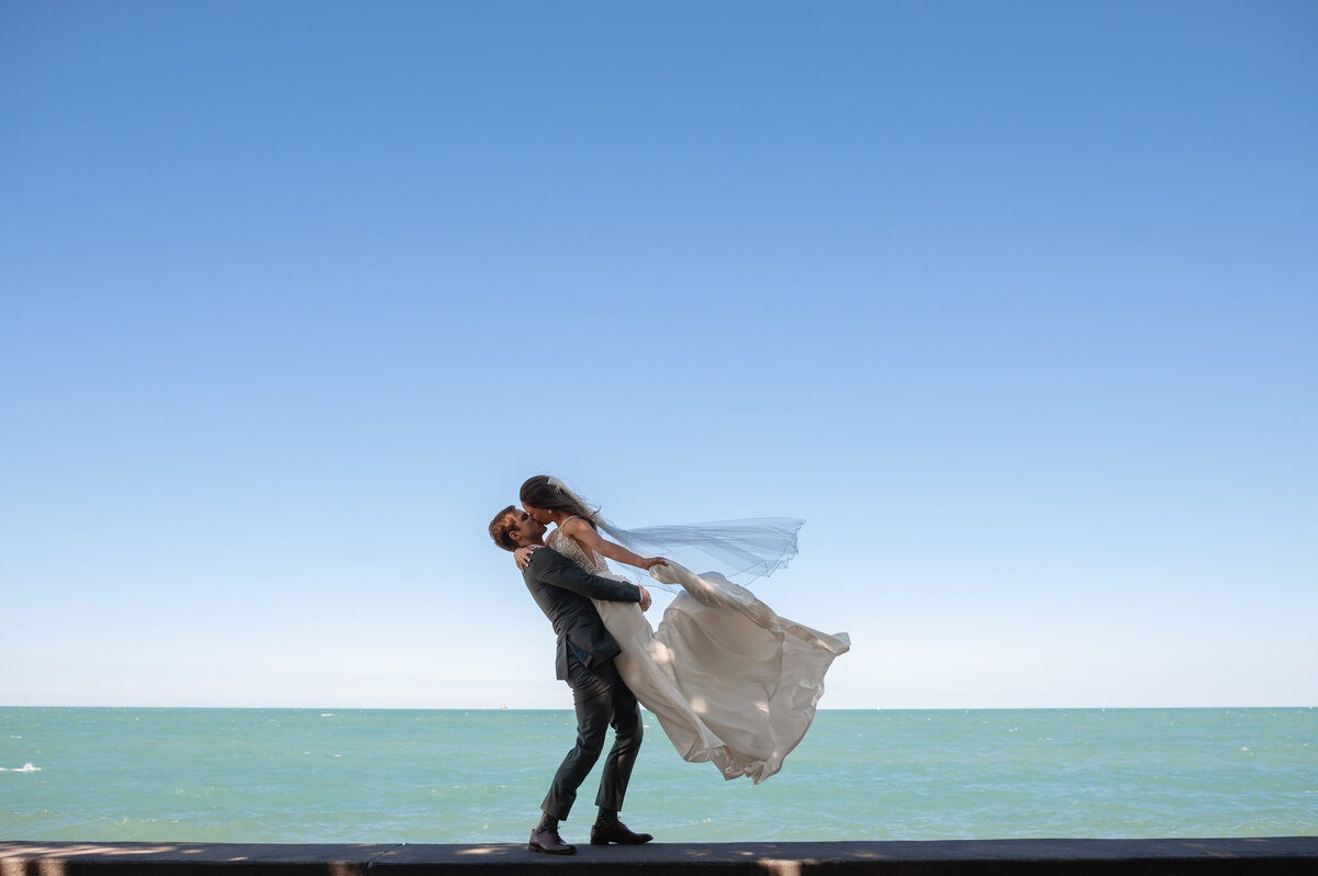 A groom picks up his bride in front of Lake Michigan in Chicago, IL