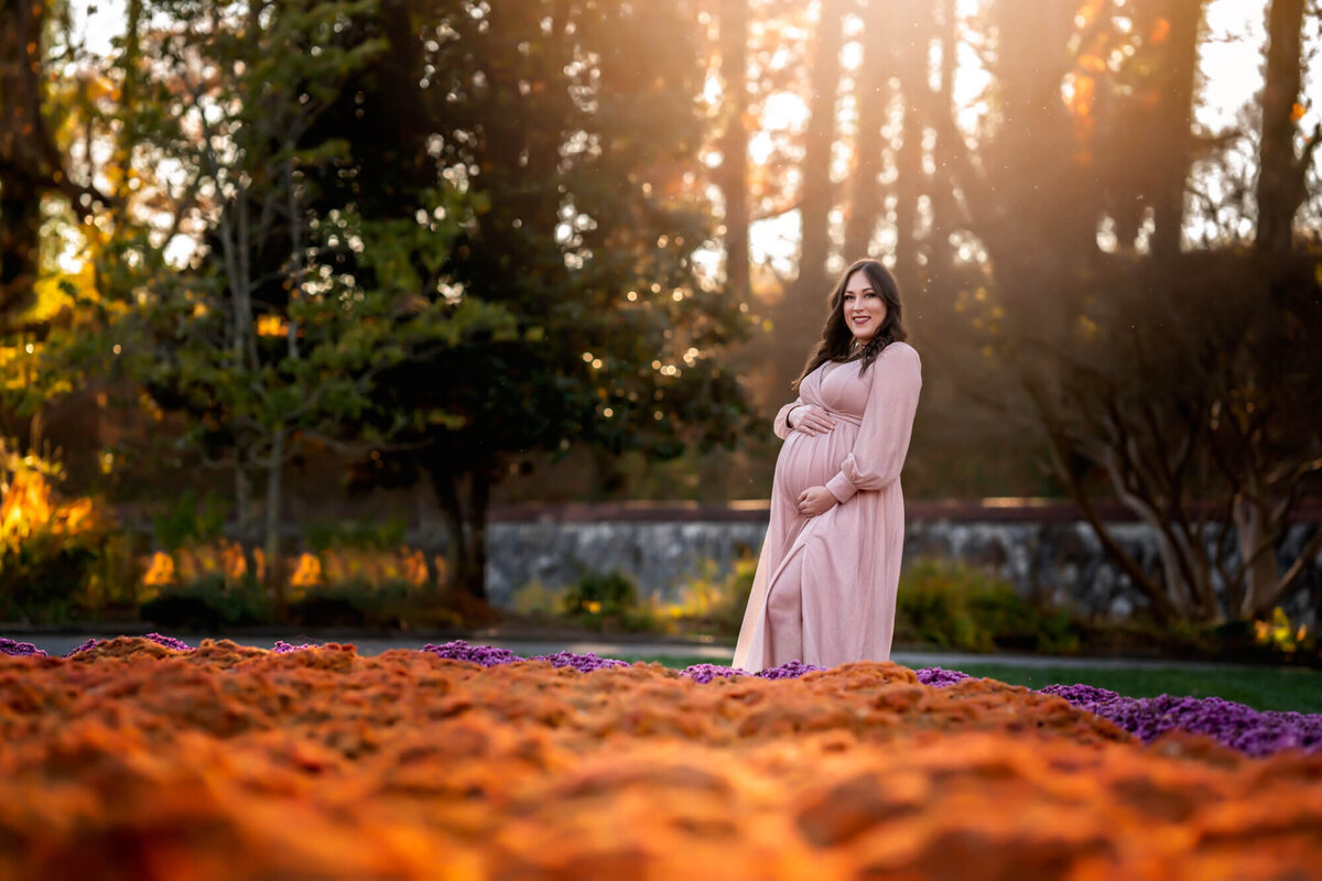 An expecting mother to be cradles her bump in front of a garden of mums