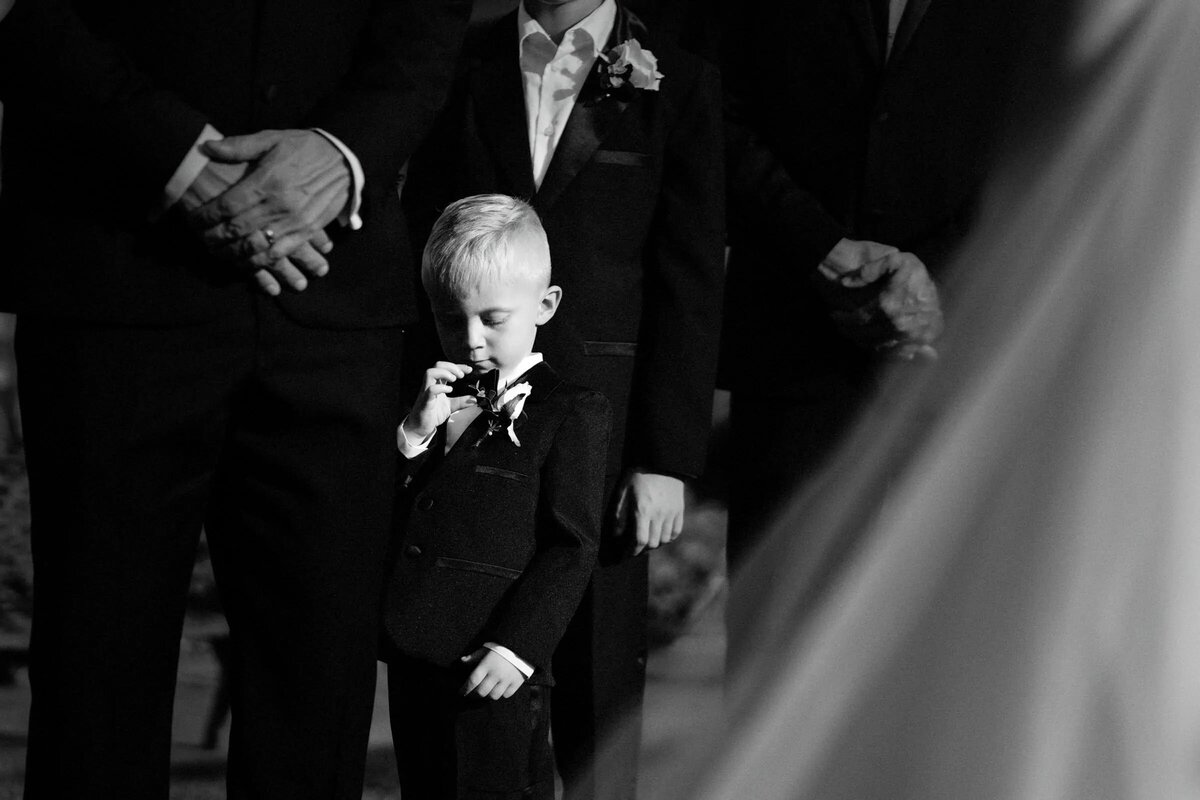 Candid black and white shot of a young pageboy adjusting his bowtie