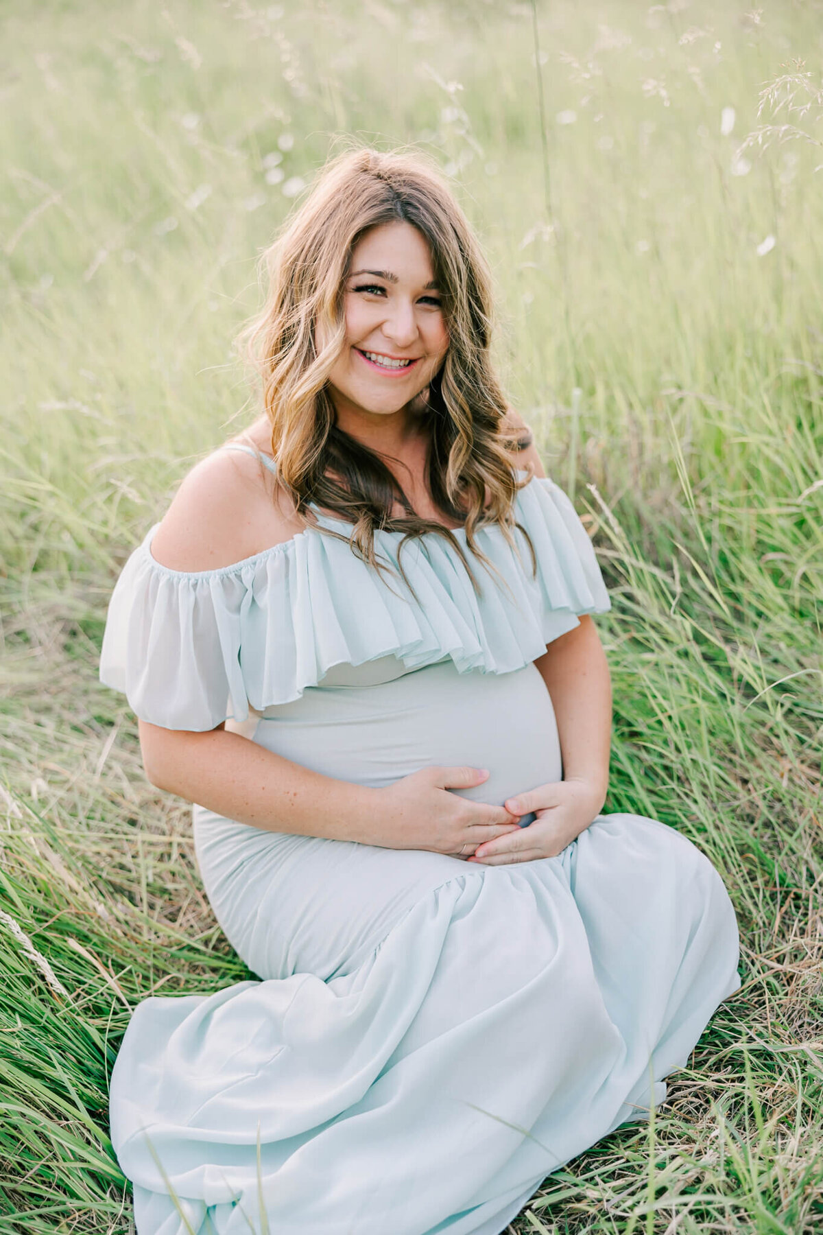 portrait of a woman smiling during her maternity photography session. She is smiling at the camera and wearing a green dress