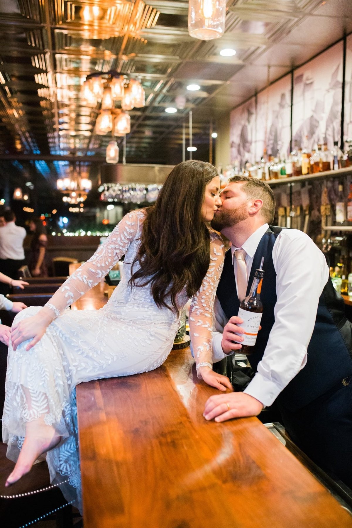Wedding Photographer, bride sitting on bar kissing groom