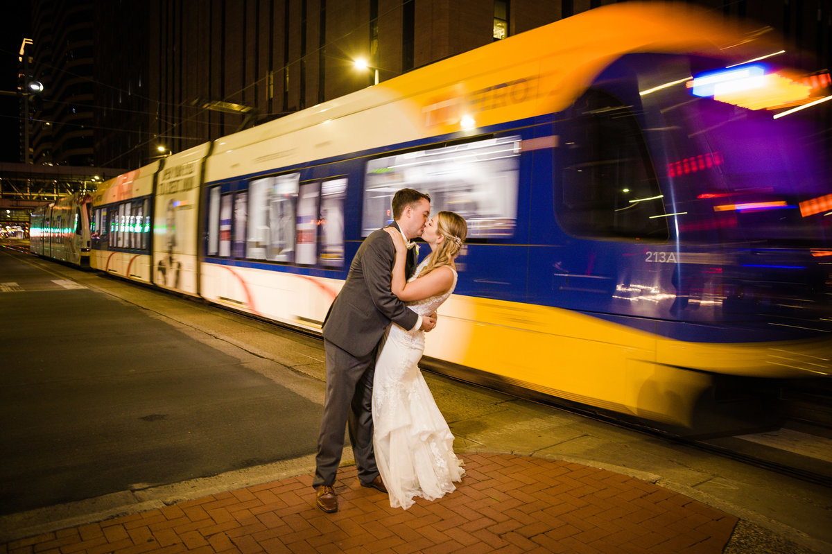 Bride and groom kiss in  front of the Light Rail in Minneapolis, Minnesota.