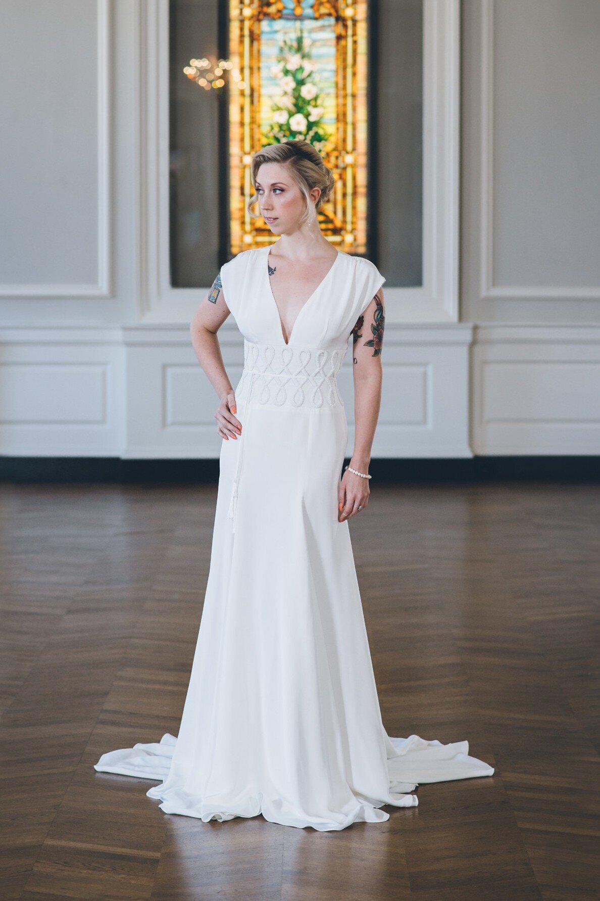 The Anila style is a sheath crepe wedding gown with a v-neck and hand-beaded waistline.