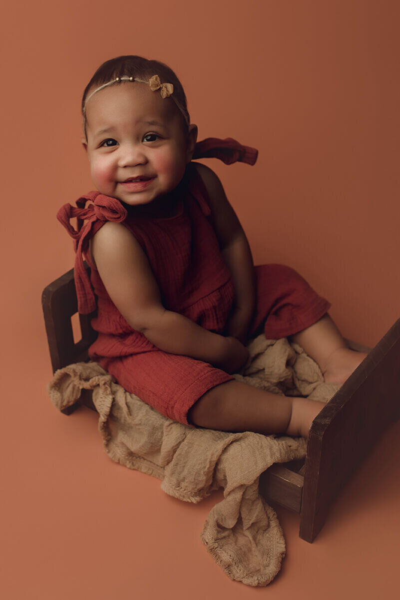 a one year old girl who is happy and smiling on a wooden bed