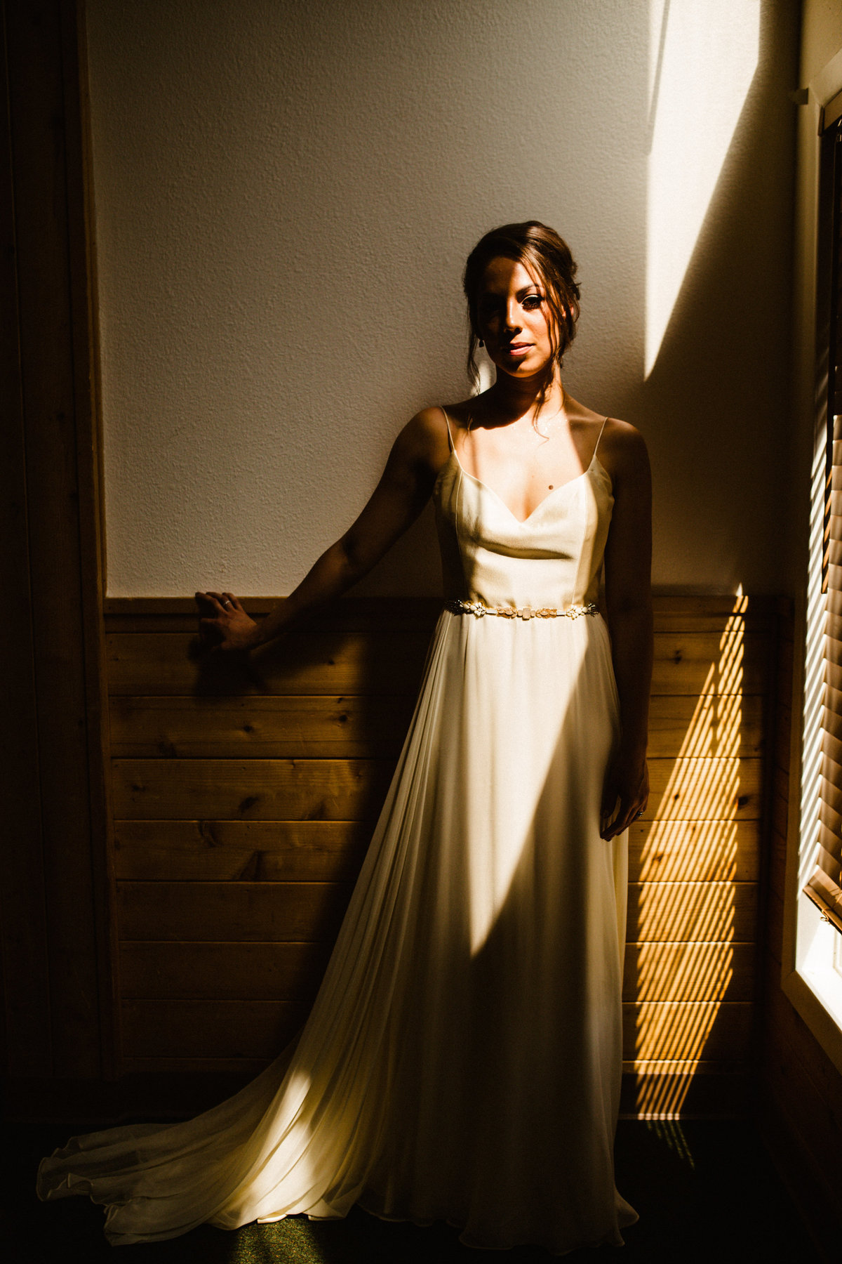 bride stands in stark sun patch of light at otter lake lodge