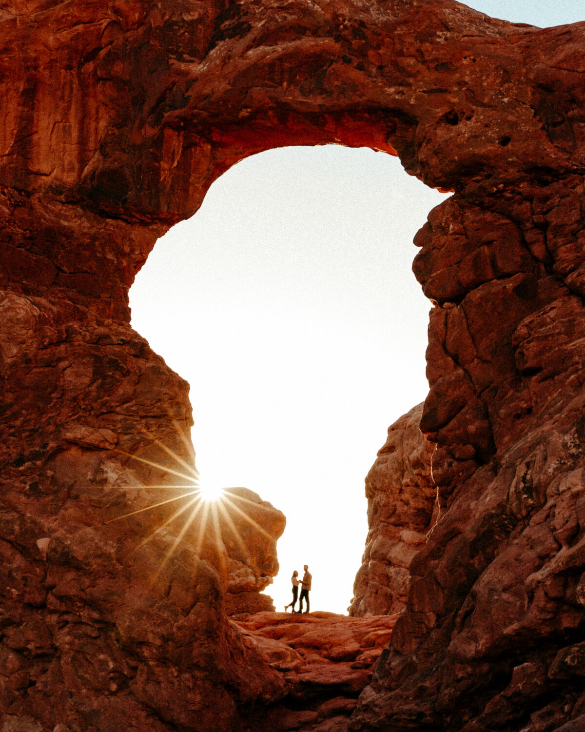Silhouetted couple standing in Turret arch in Arches National Park at sunset