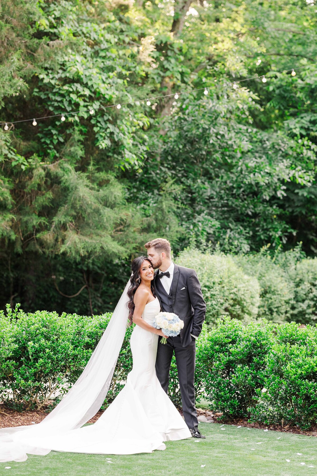 Groom kissing bride on forehead while bride laughs for the photo at the Barn at Firefly Lane