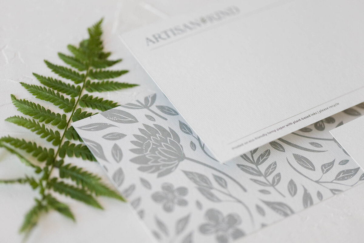 Floral pattern branded note card next to a stem of a fern